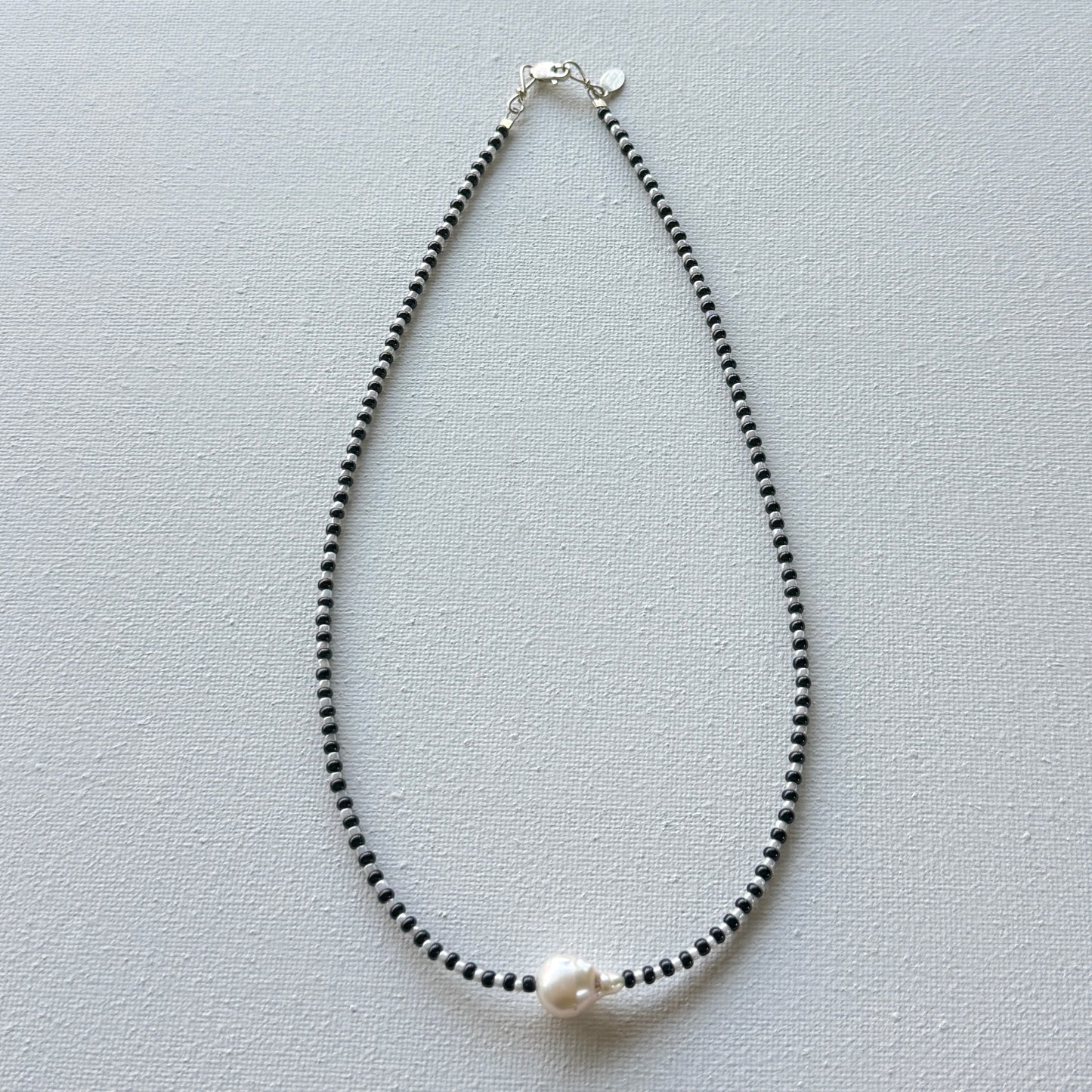 Necklace with black beads and a pearl on a light gray background