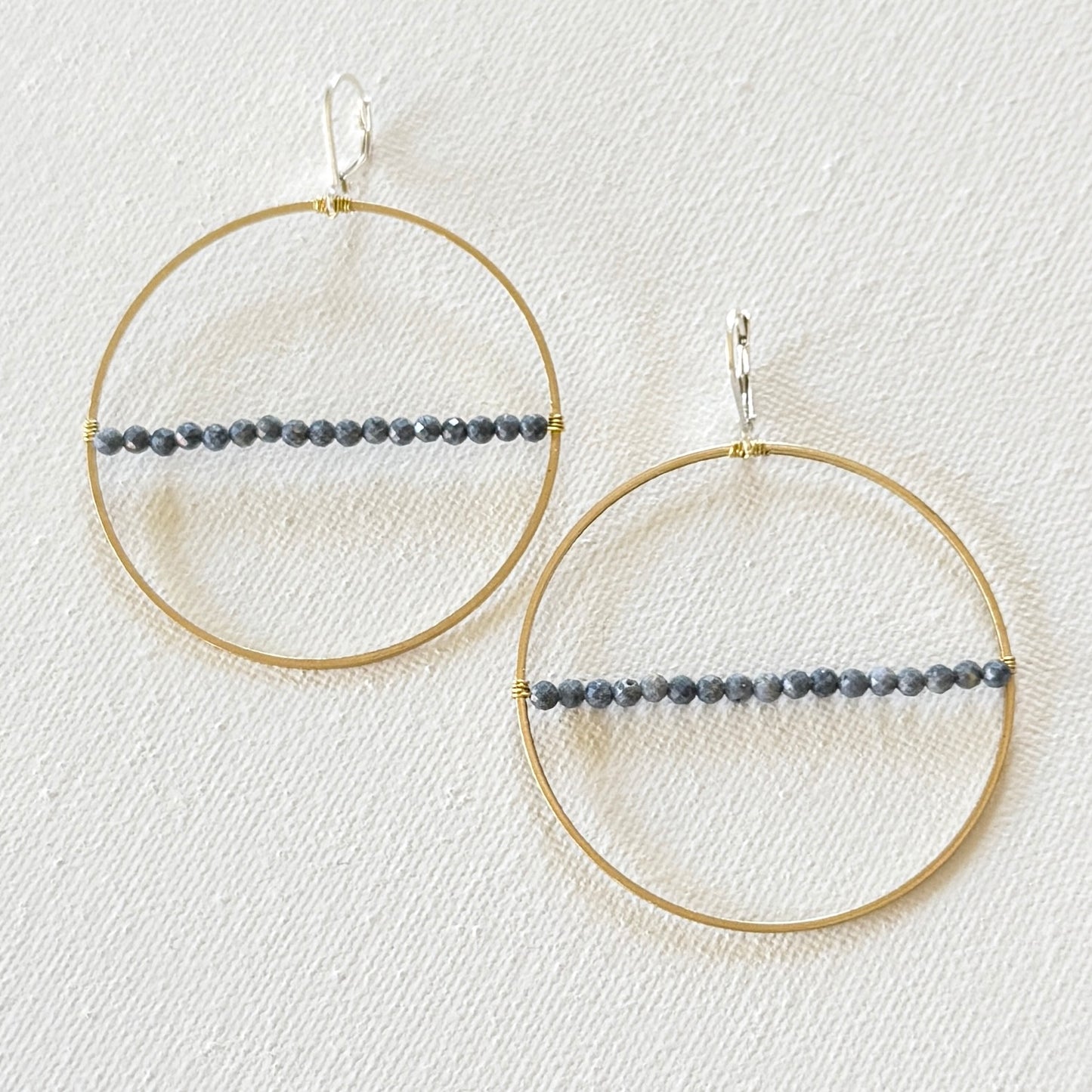 Gold hoop earrings with beaded extensions on a textured white surface