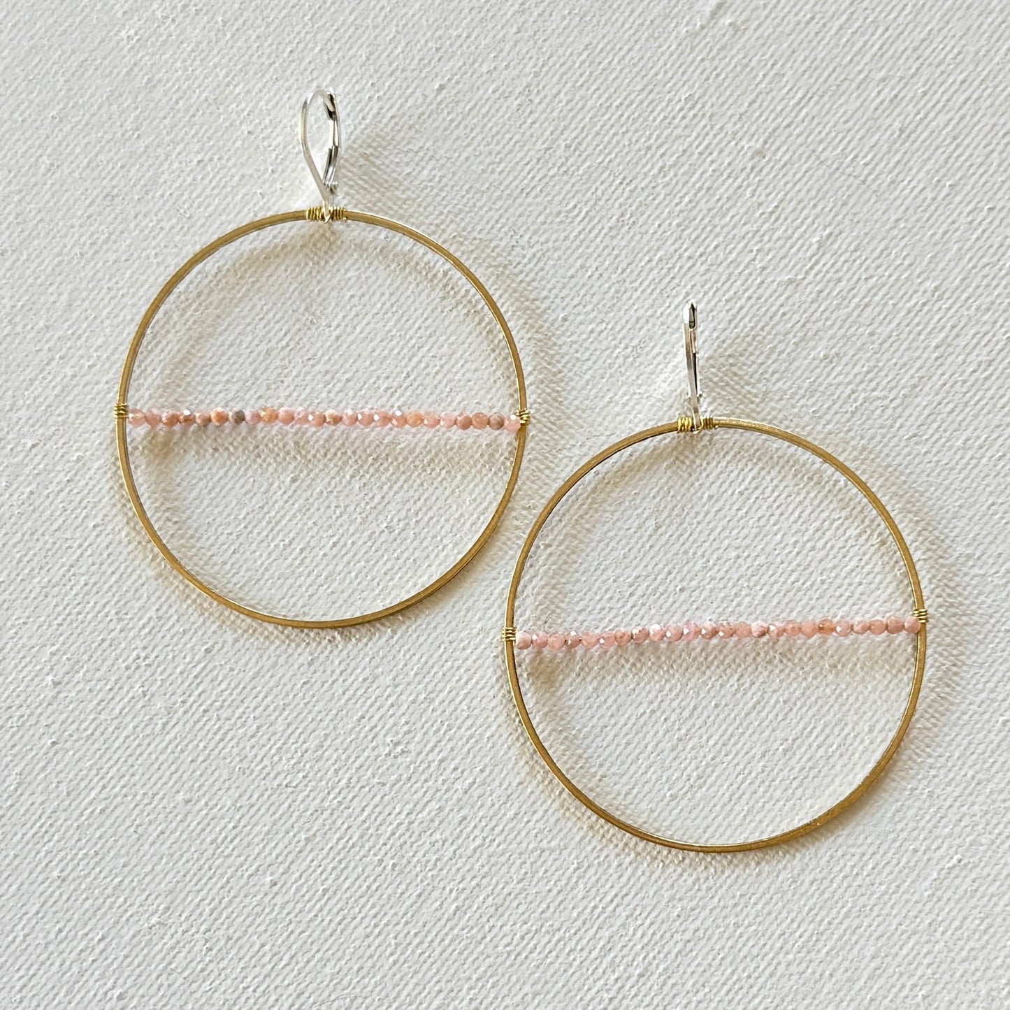 Gold hoop earrings with pink beads on a light gray background