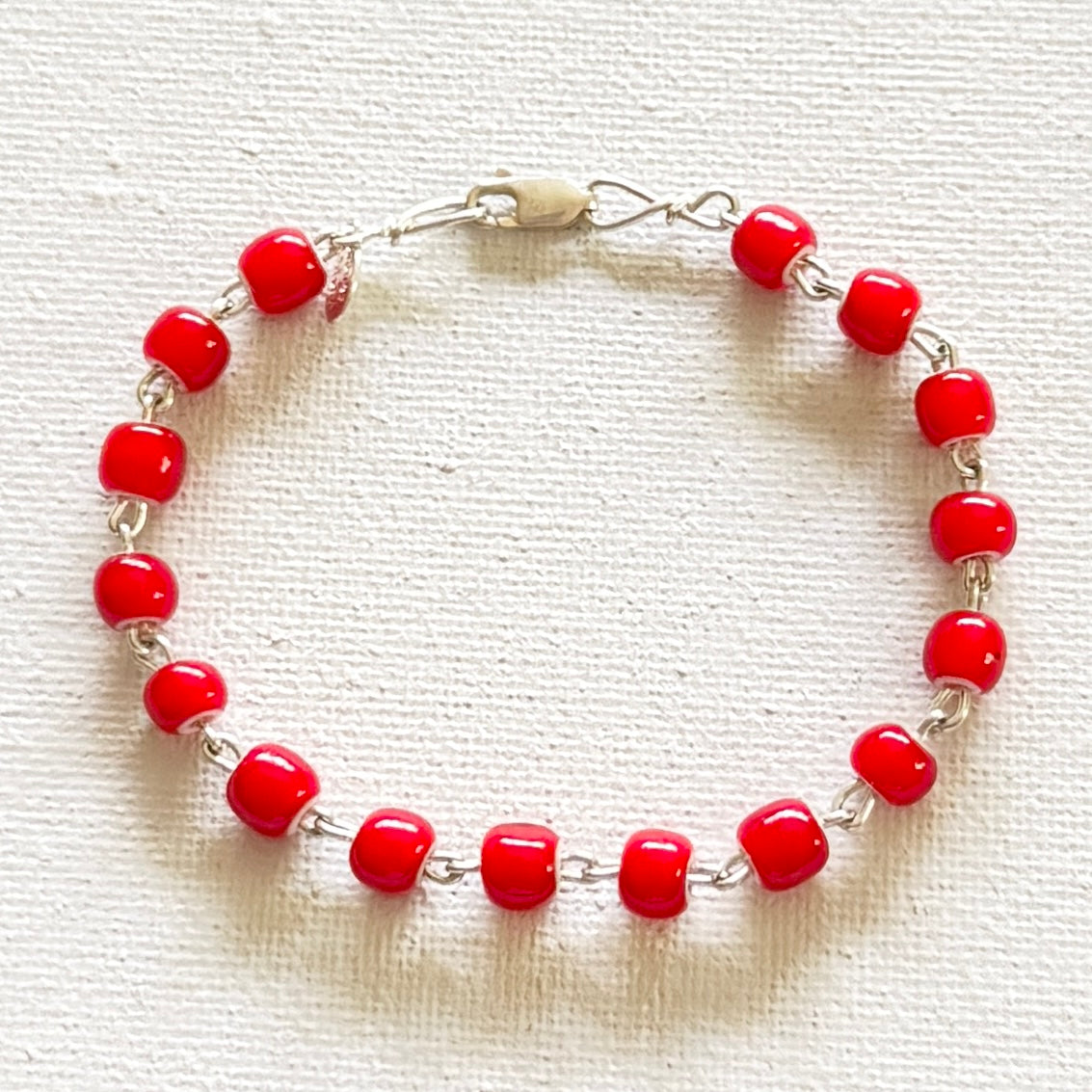red glossy cylindrical beads linked with silver color and a textured white back ground.