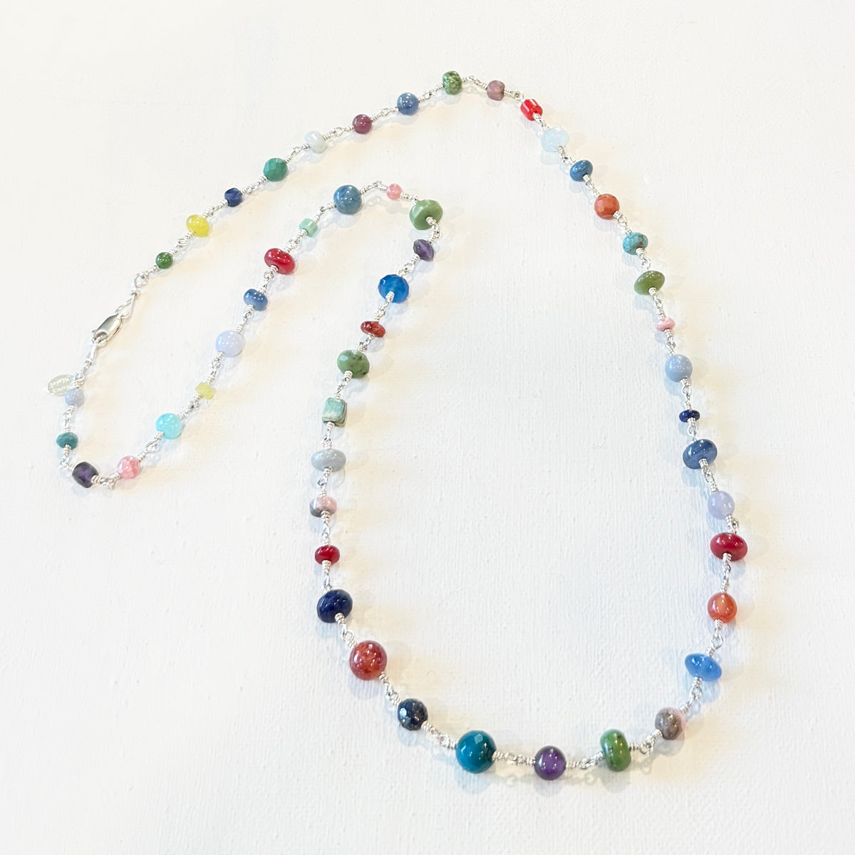 A beaded necklace made of small round multicolor gemstone beads separated by silver-toned metal links, displayed on a plain off-white background.
