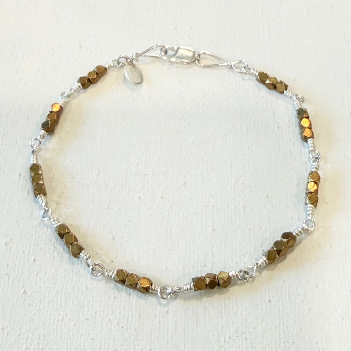 A beaded bracelet featuring faceted brown beads and silver-toned wire wrapping and chain clasp, displayed on a textured off-white background.