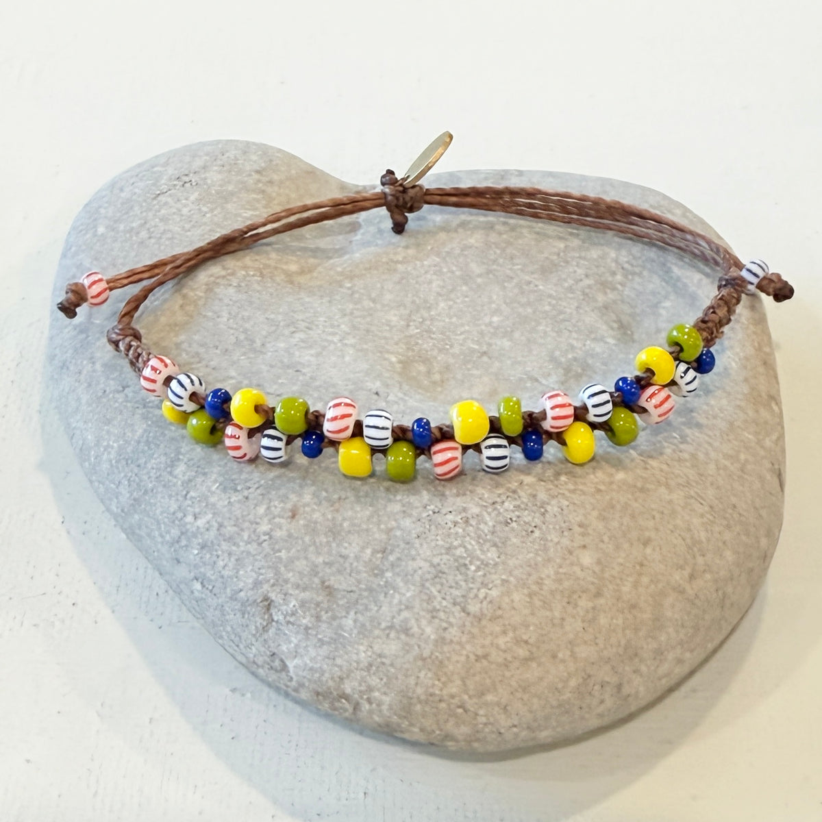 A handmade beaded necklace with a brown adjustable cord and colorful round beads, displayed on a smooth gray stone against a plain white background.