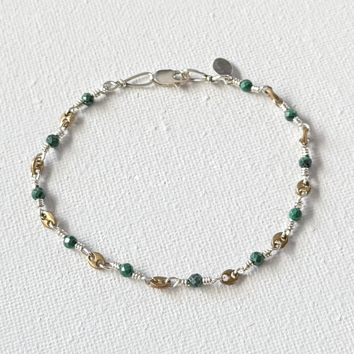 Beaded bracelet with green faceted turquoise and gold beads on a white fabric background.