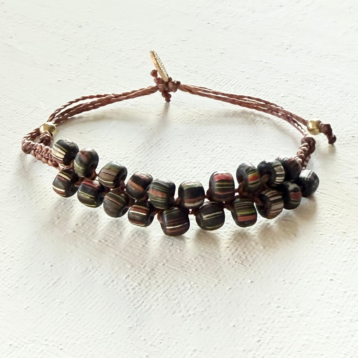 Beaded bracelet with brown cord on a white fabric background