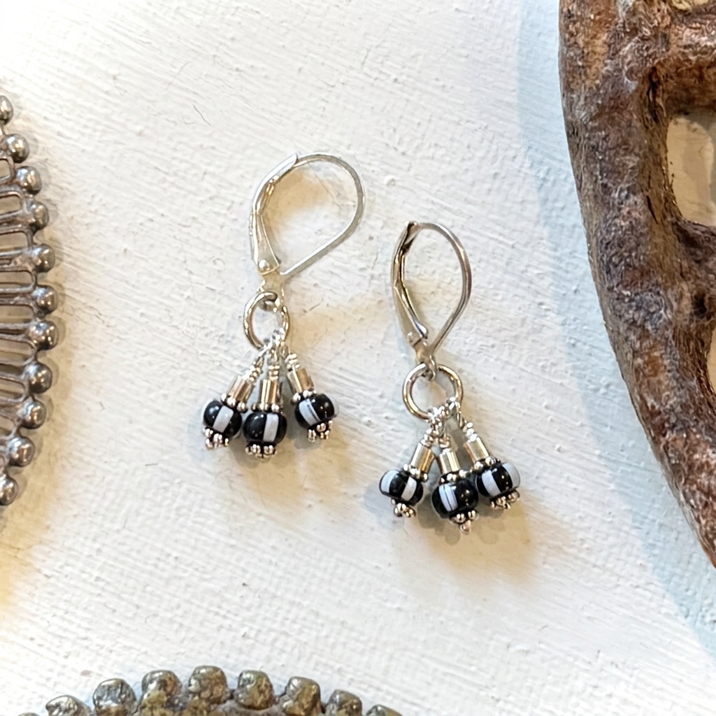 A pair of silver leverback dangle earrings with small black and white bead clusters, displayed on a textured white surface with rustic wood props.