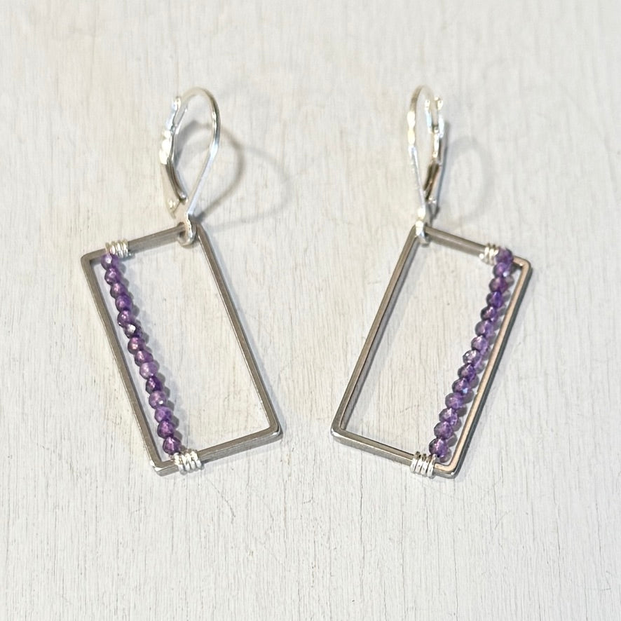 Pair of silver earrings with purple beads on a light wooden background