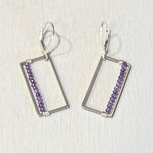 Pair of silver earrings with purple beads on a light wooden background