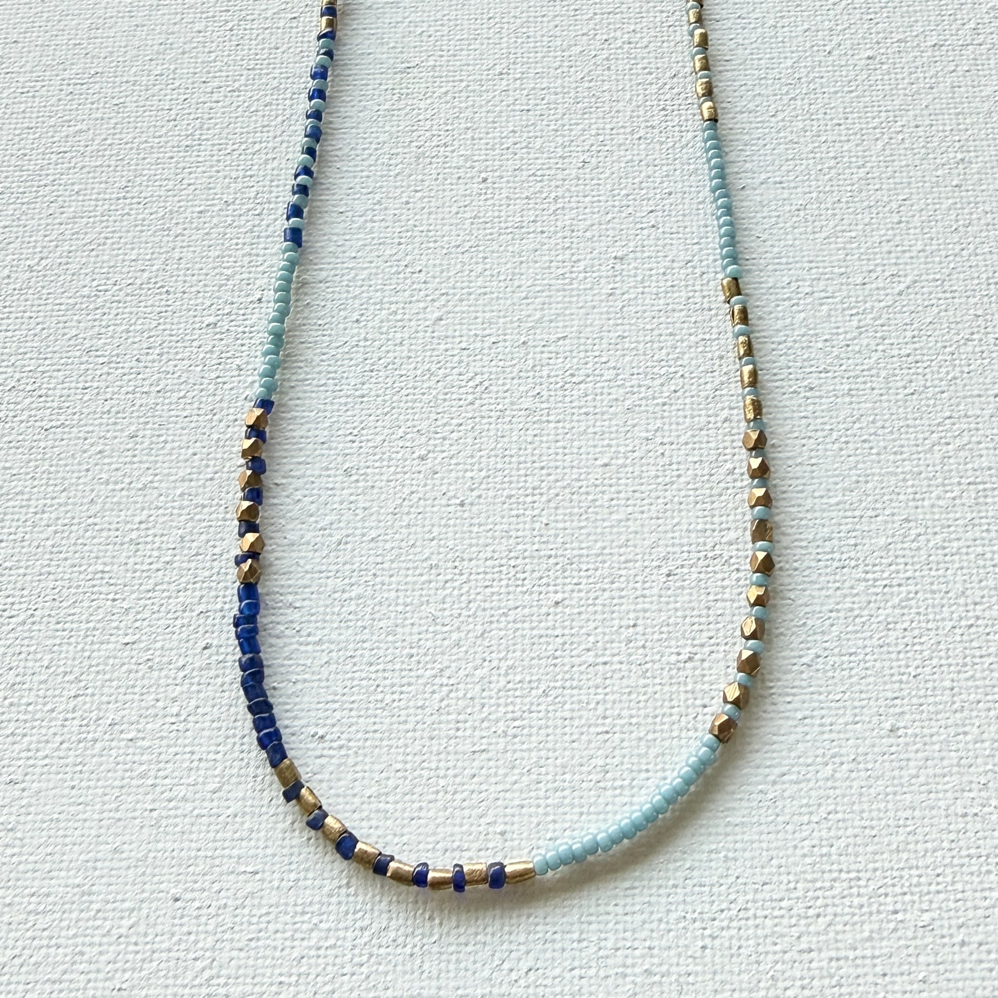 Beaded necklace with blue, gold, and silver beads on a light gray background