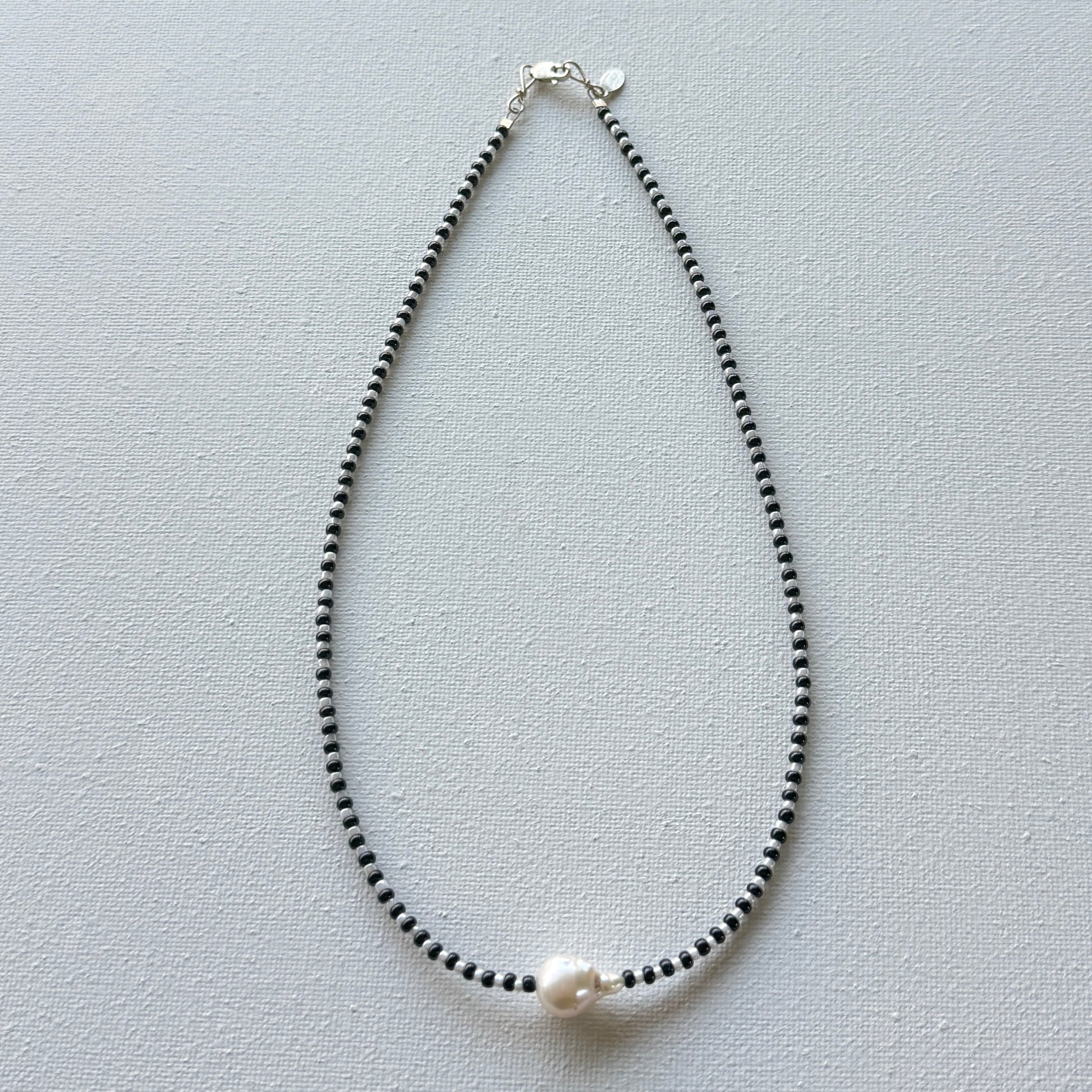 Necklace with black beads and a pearl on a light gray background