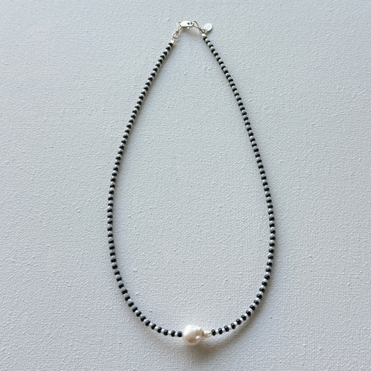 Necklace with black beads and a pearl on a light gray background