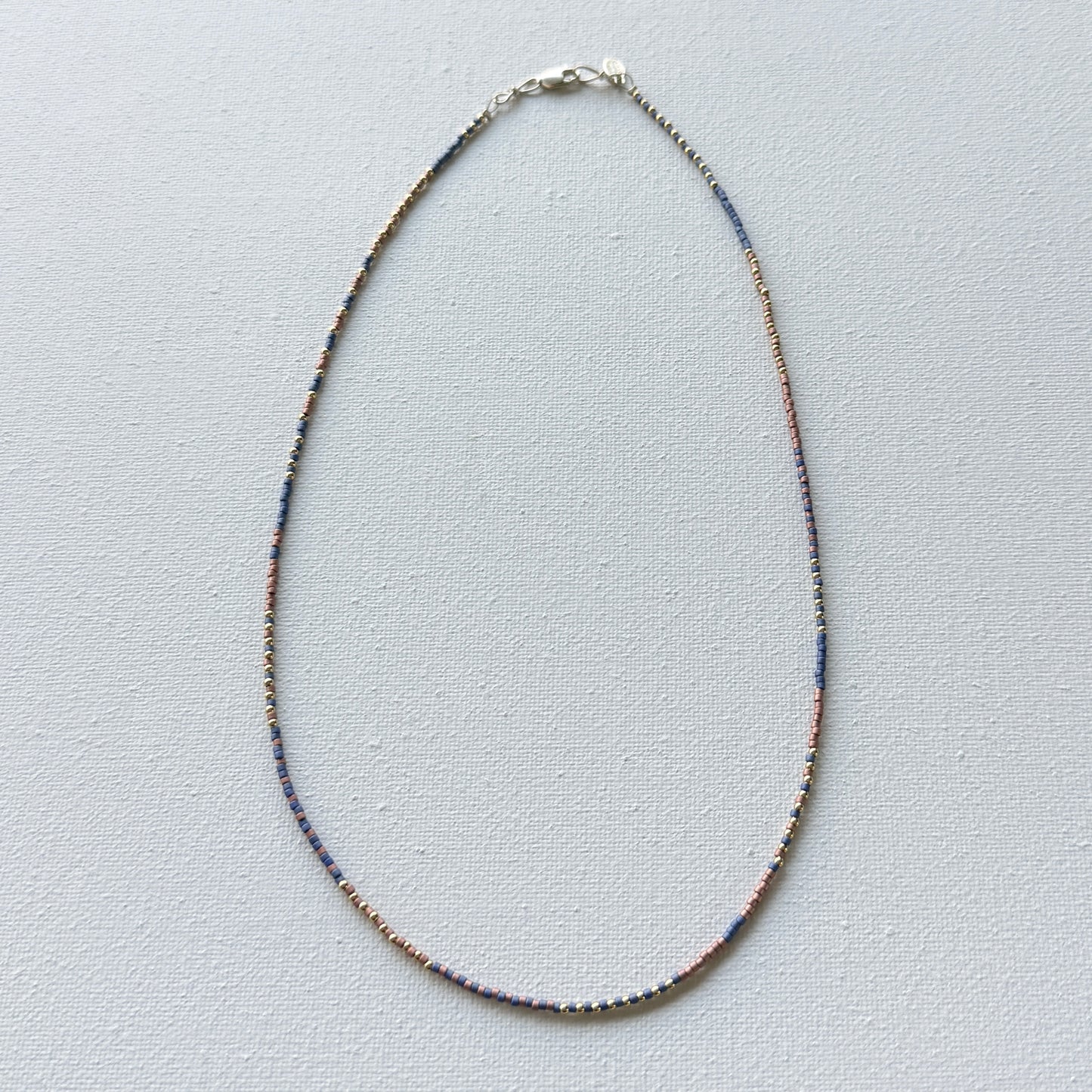 Thin beaded necklace with copper, brass and denim beads on a light gray background