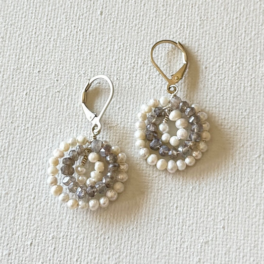 Pair of beaded earrings on a textured white background. With white freshwater pearls and grey faceted labradorite gemstones.