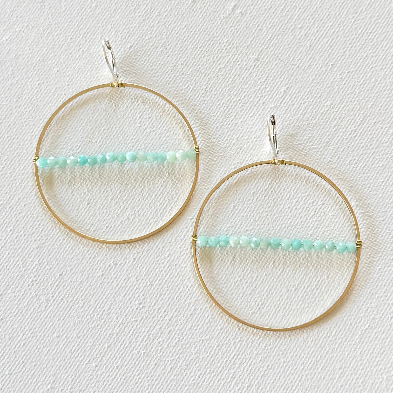 Gold hoop earrings with turquoise beads on a light background