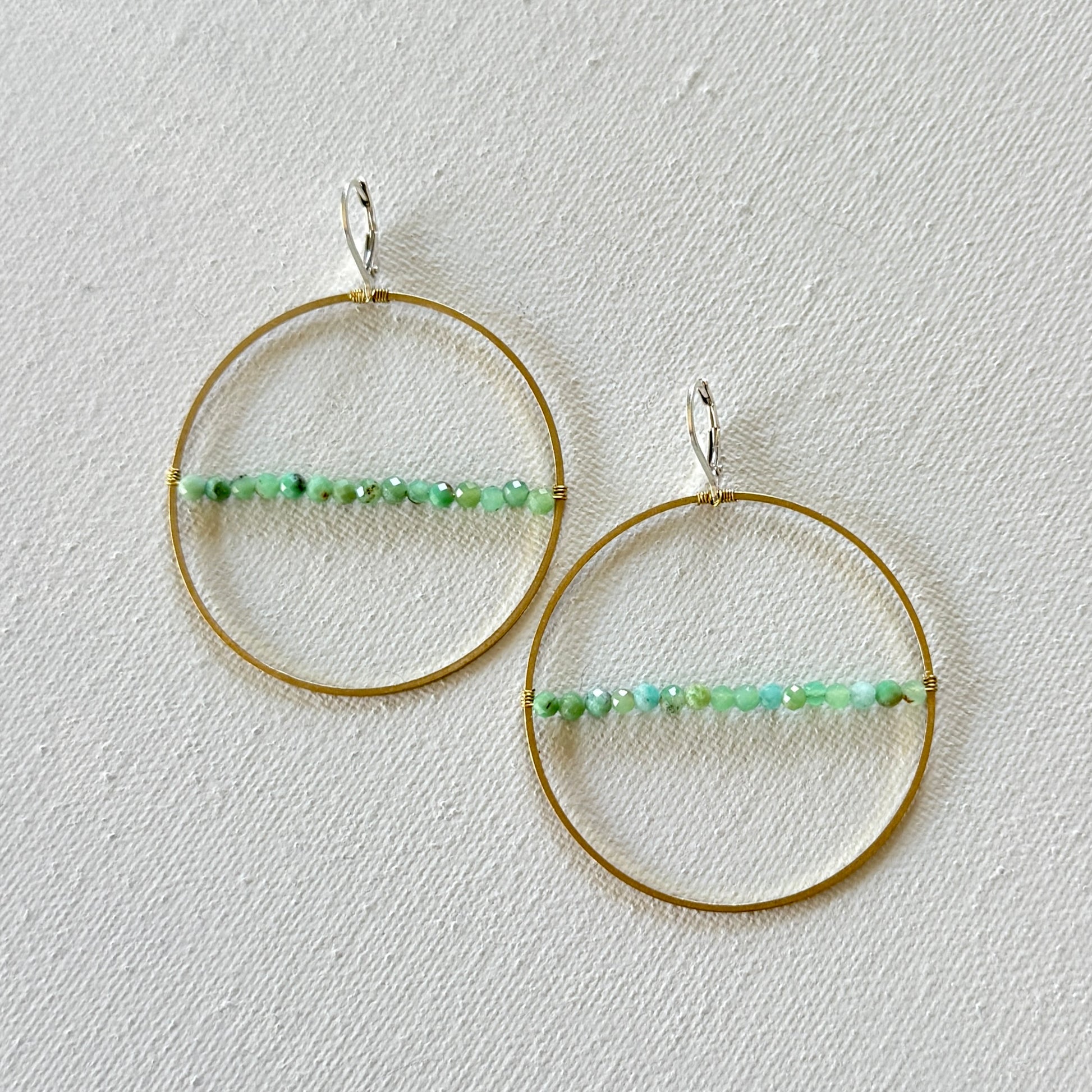 Gold hoop earrings with green bead accents on a light gray background