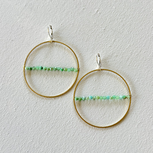 Gold hoop earrings with green bead accents on a light gray background