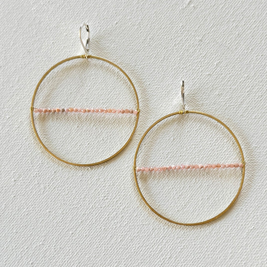 Gold hoop earrings with pink beads on a light gray background