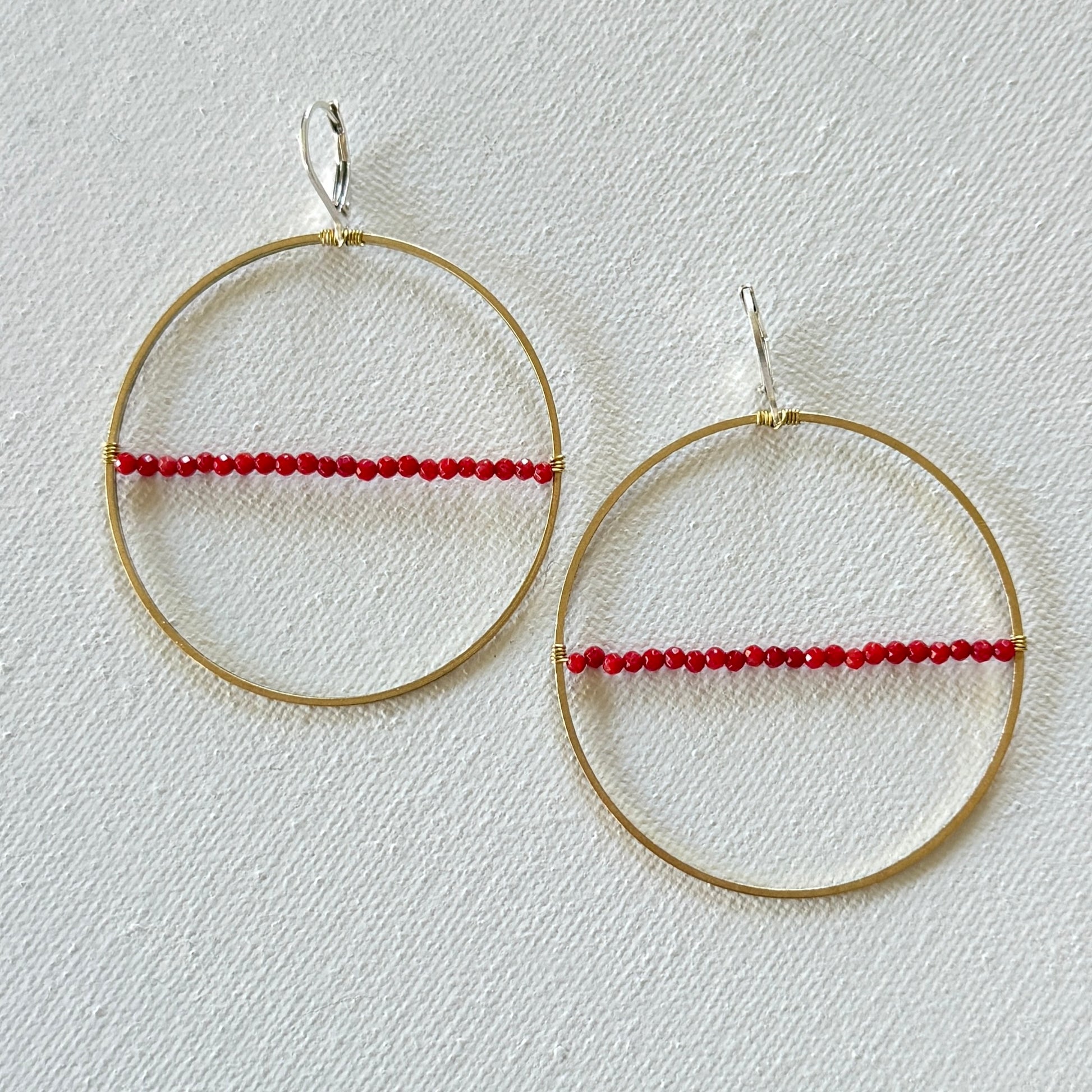Gold hoop earrings with red beads on a light gray background