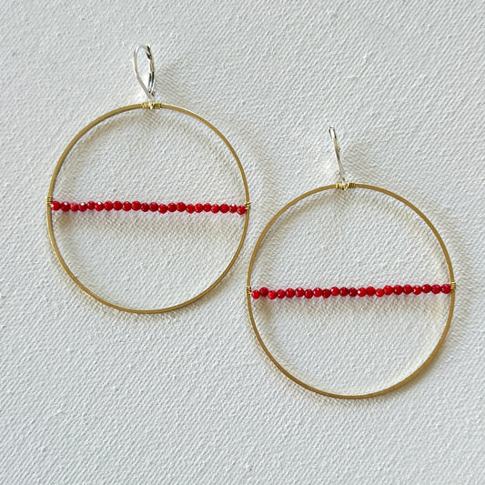 Gold hoop earrings with red beads on a light gray background