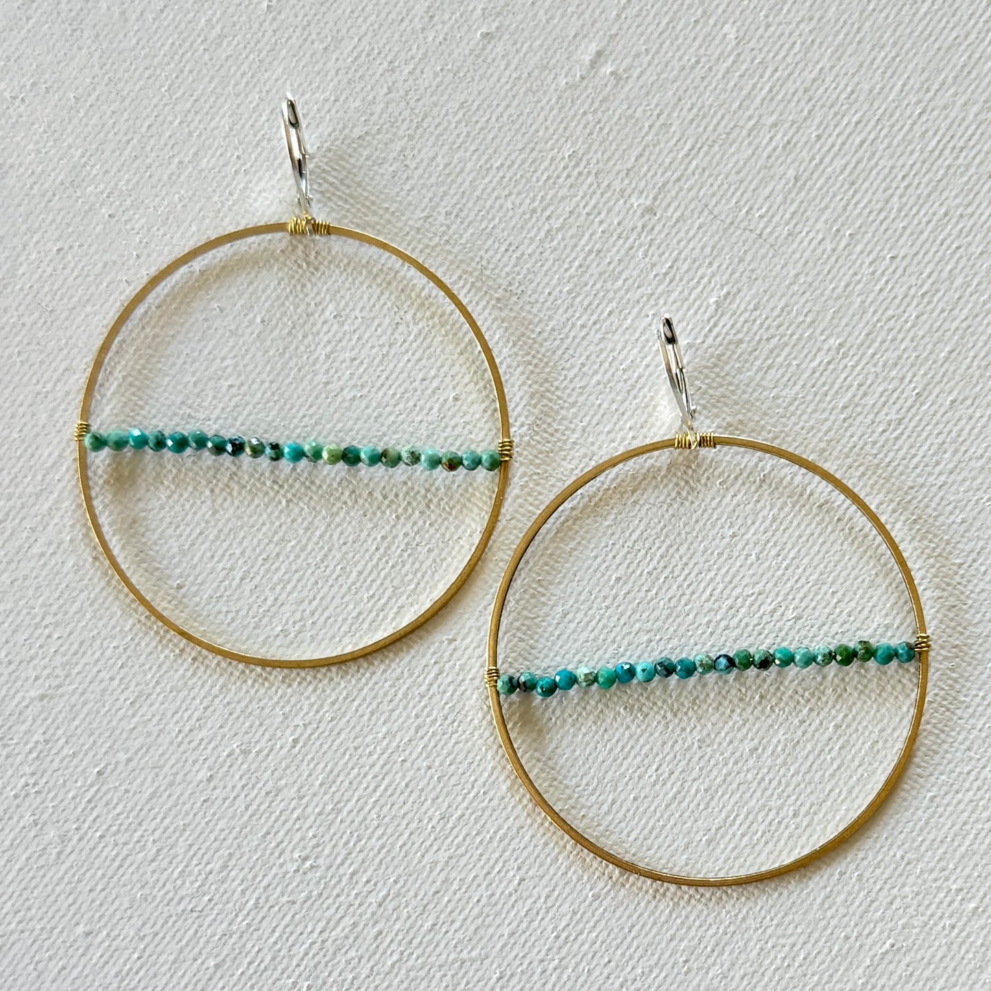 Gold hoop earrings with green beads on a textured white background