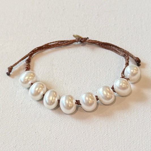 Pearl bracelet with brown cord on a light background. The pearls are potato shape in white.