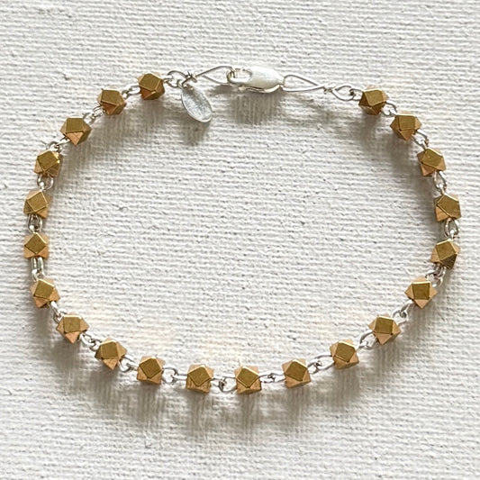 A delicate bracelet made of faceted gold beads linked by silver-toned metal rings, featuring a silver clasp with a small white inlay, displayed on a textured white background.