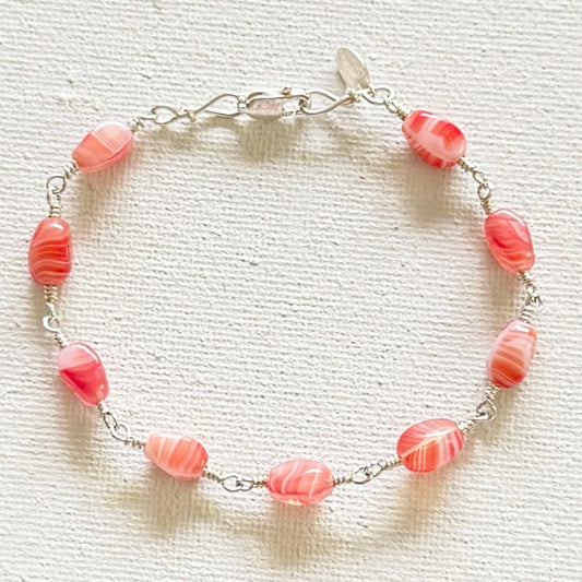 A silver hand linked bracelet featuring multiple red and white marbled beads, displayed on a textured off-white fabric background.