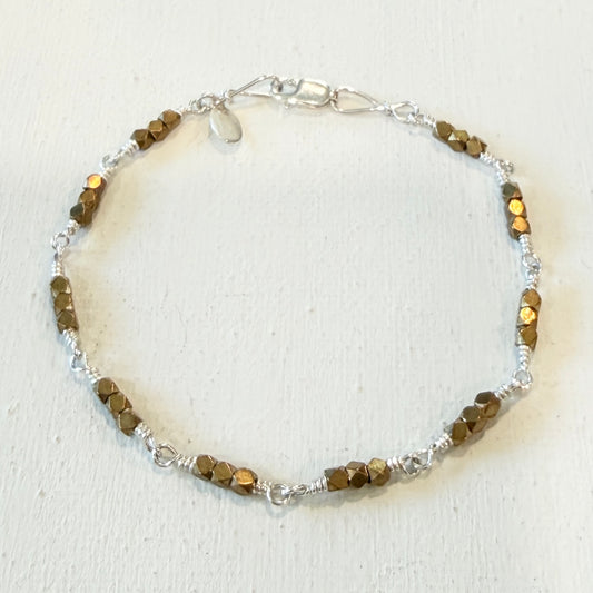 A beaded bracelet featuring faceted brown beads and silver-toned wire wrapping and chain clasp, displayed on a textured off-white background.