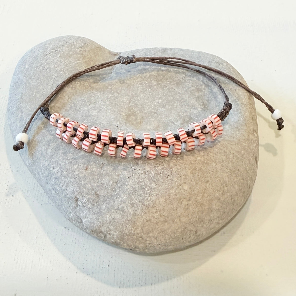 A beaded stretch bracelet with pink and white striped beads on a dark brown cord, displayed on a smooth gray stone against a light background.