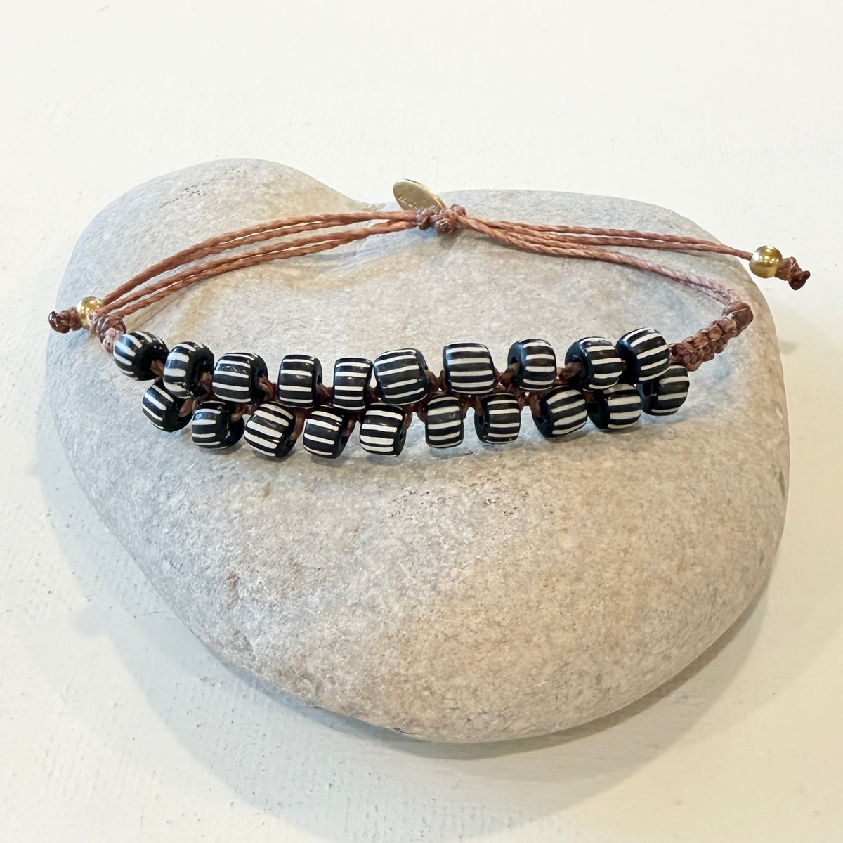 A handmade adjustable cord bracelet with black and white striped beads, displayed on a smooth light gray stone against a white background.