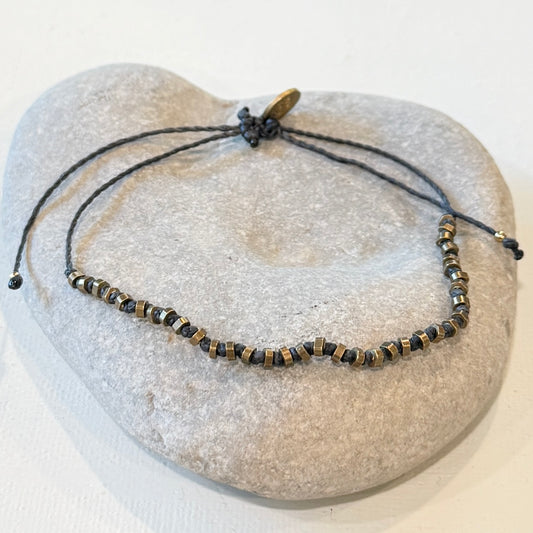 A beaded adjustable cord bracelet with metallic bronze displayed on a light gray stone stand against a white background.