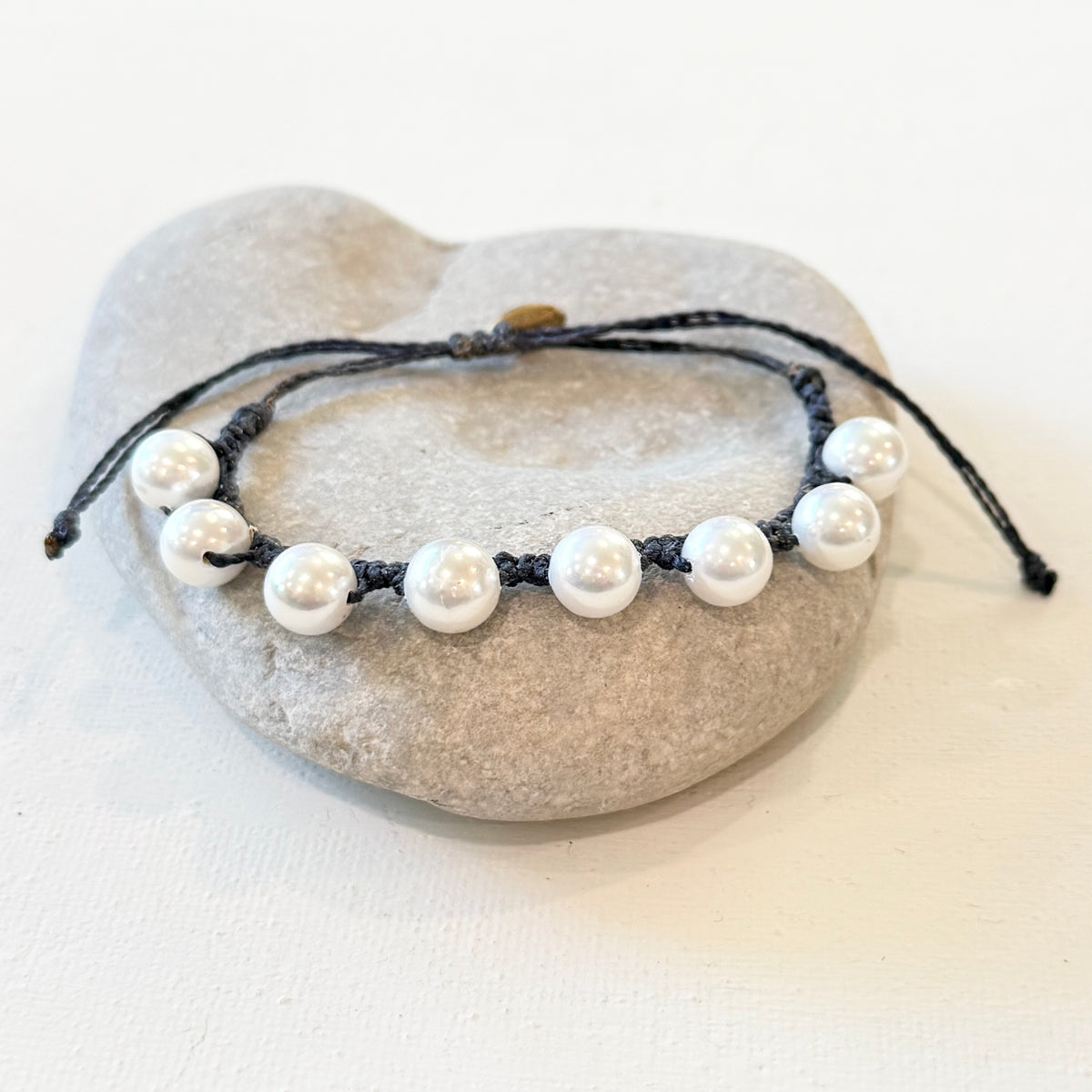 A beaded bracelet with white pearl-like beads on a black cord, displayed on a light gray stone stand against a white background.