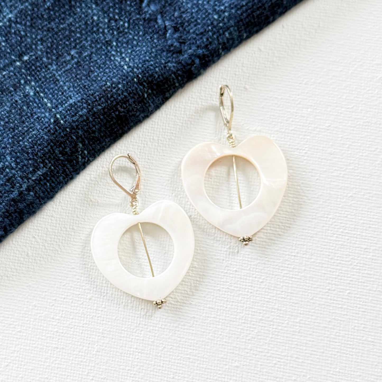 White heart-shaped earrings on a white surface with a blue fabric background. 