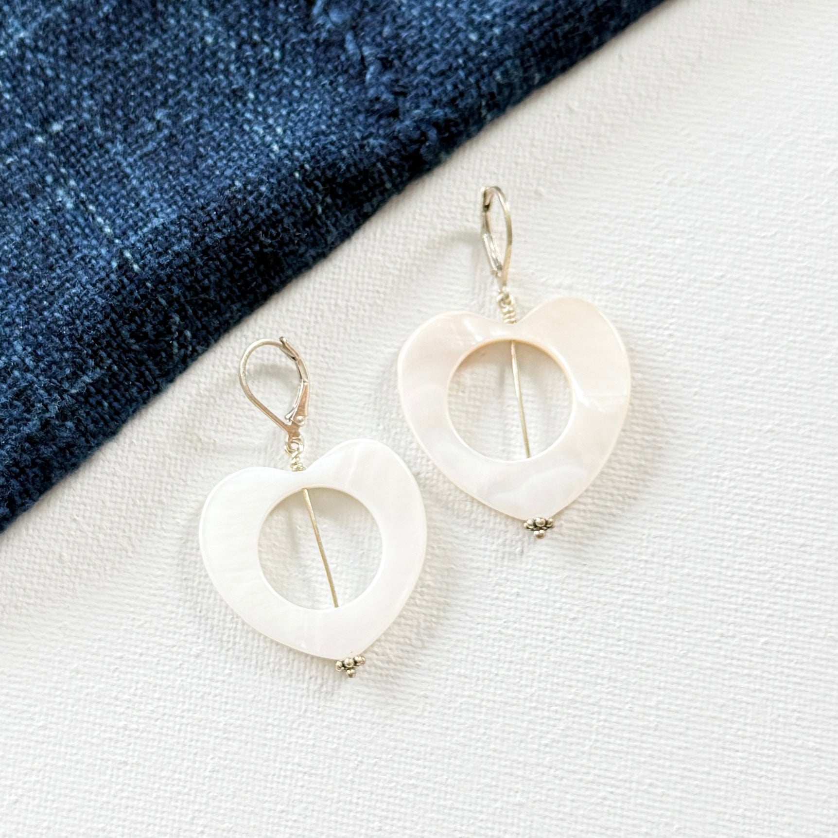 White heart-shaped earrings on a white surface with a blue fabric background. 