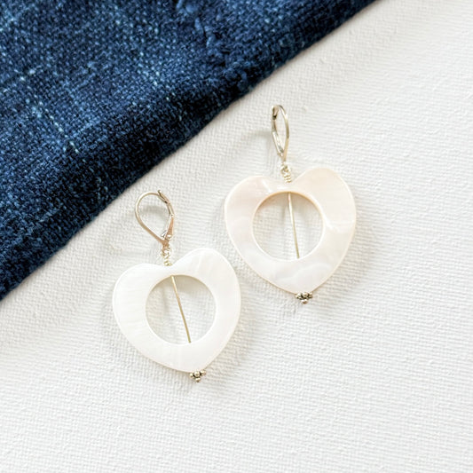 White heart-shaped earrings on a white surface with a blue fabric background. 