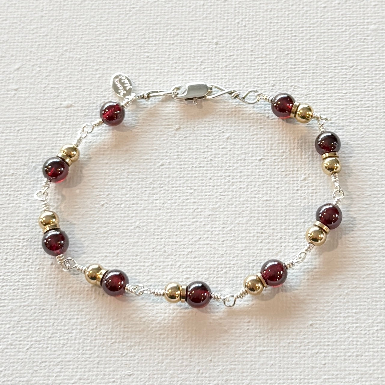 hand linked sterling silver with a sterling silver lobster clasp and a hand stamped signature tag. Brass spheres connected with a brass ring and 6-7mm smooth garnet gemstones.