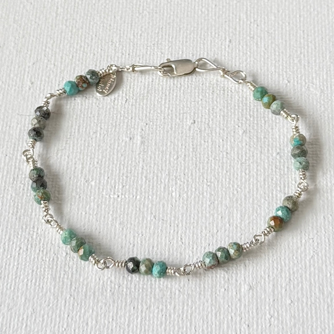 Beaded bracelet with silver clasp on a white background with faceted green turquoise beads in clusters of 3.