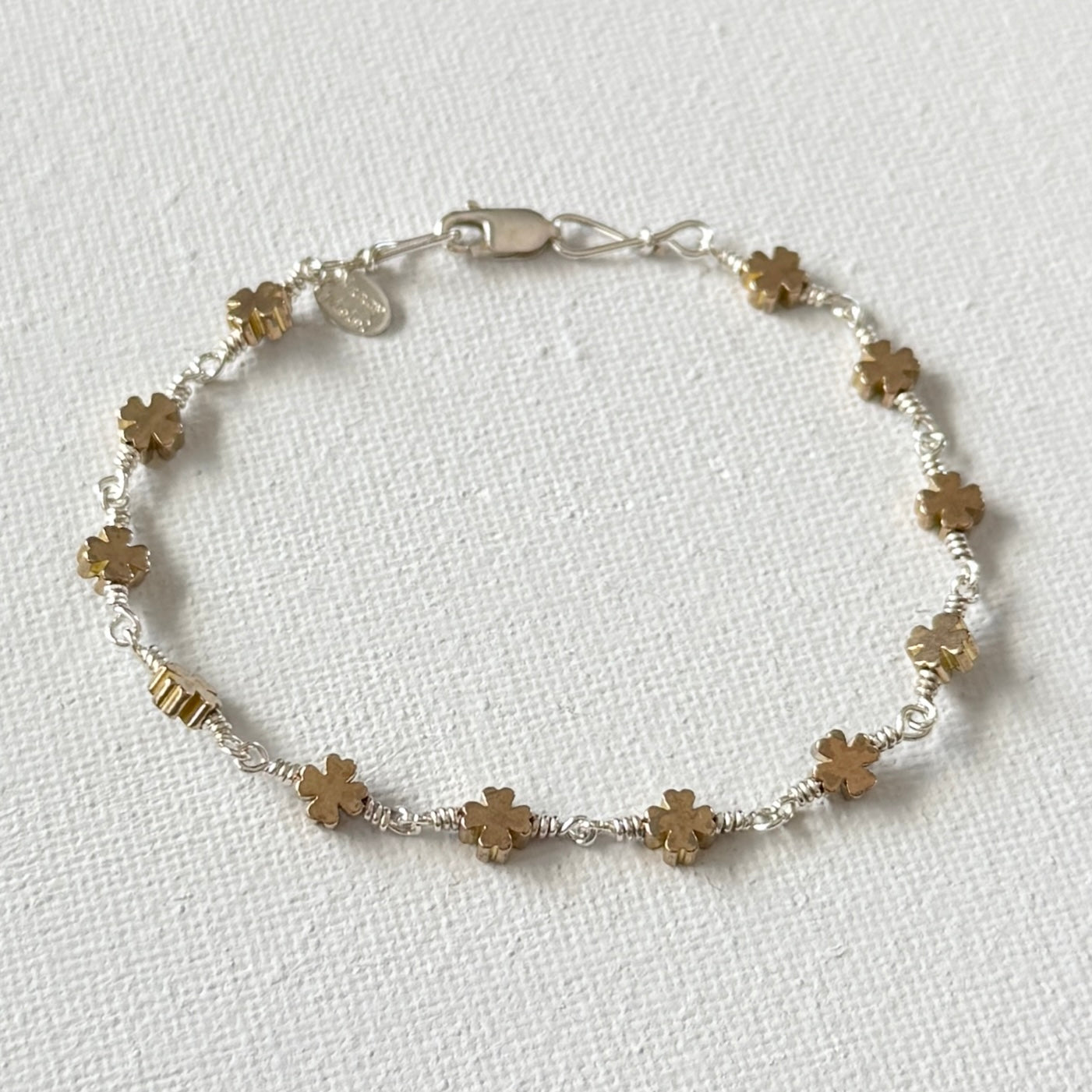 Bracelet with gold four leaf clover beads and linked with sterling silver wire with a lobster clasp on a white background.