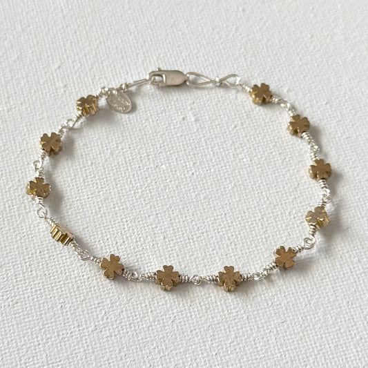 Bracelet with gold four leaf clover beads and linked with sterling silver wire with a lobster clasp on a white background.