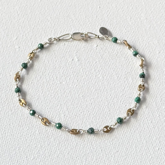 Beaded bracelet with green  faceted turquoise and gold beads on a white fabric background.