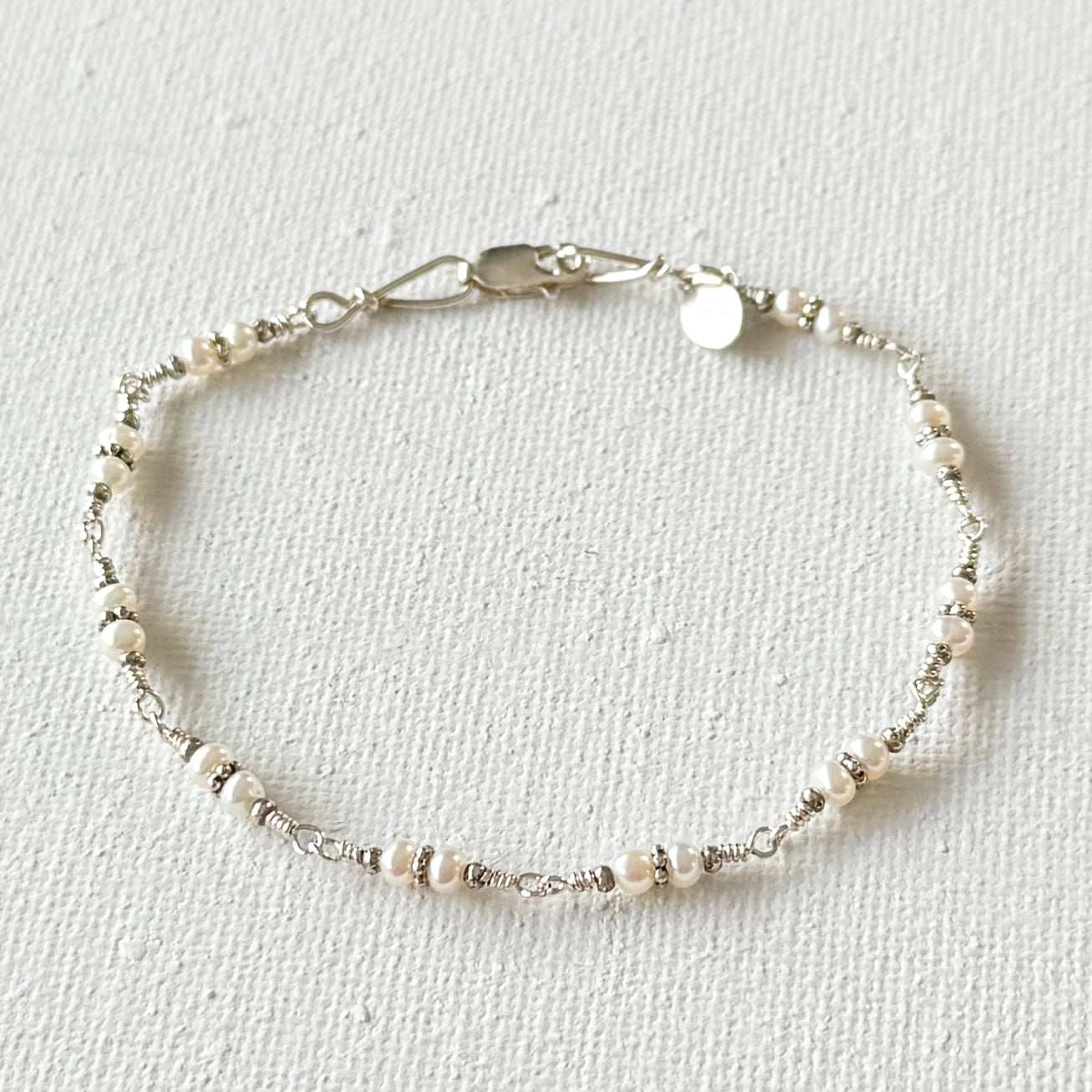 Delicate bracelet with pearls and silver on a light gray background.