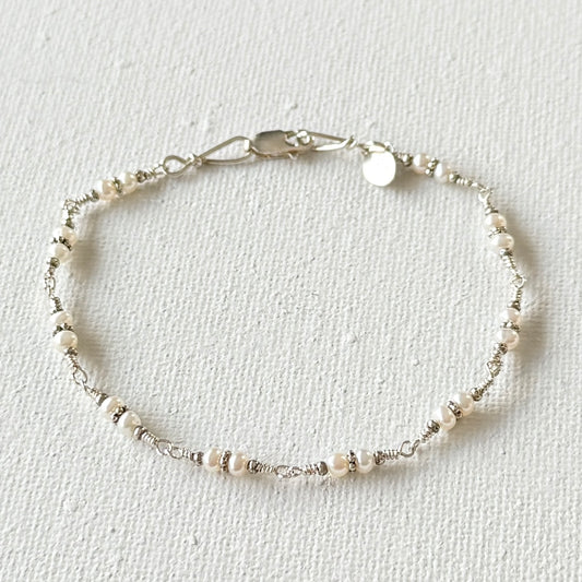 Delicate bracelet with pearls and silver on a light gray background.