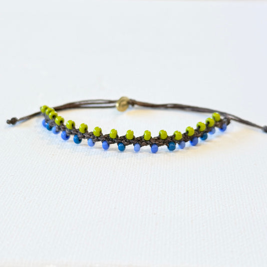 blue and green tiny seed beads linked with chocolate brown waxed nylon. Adjustable in size with a brass monogram tag.