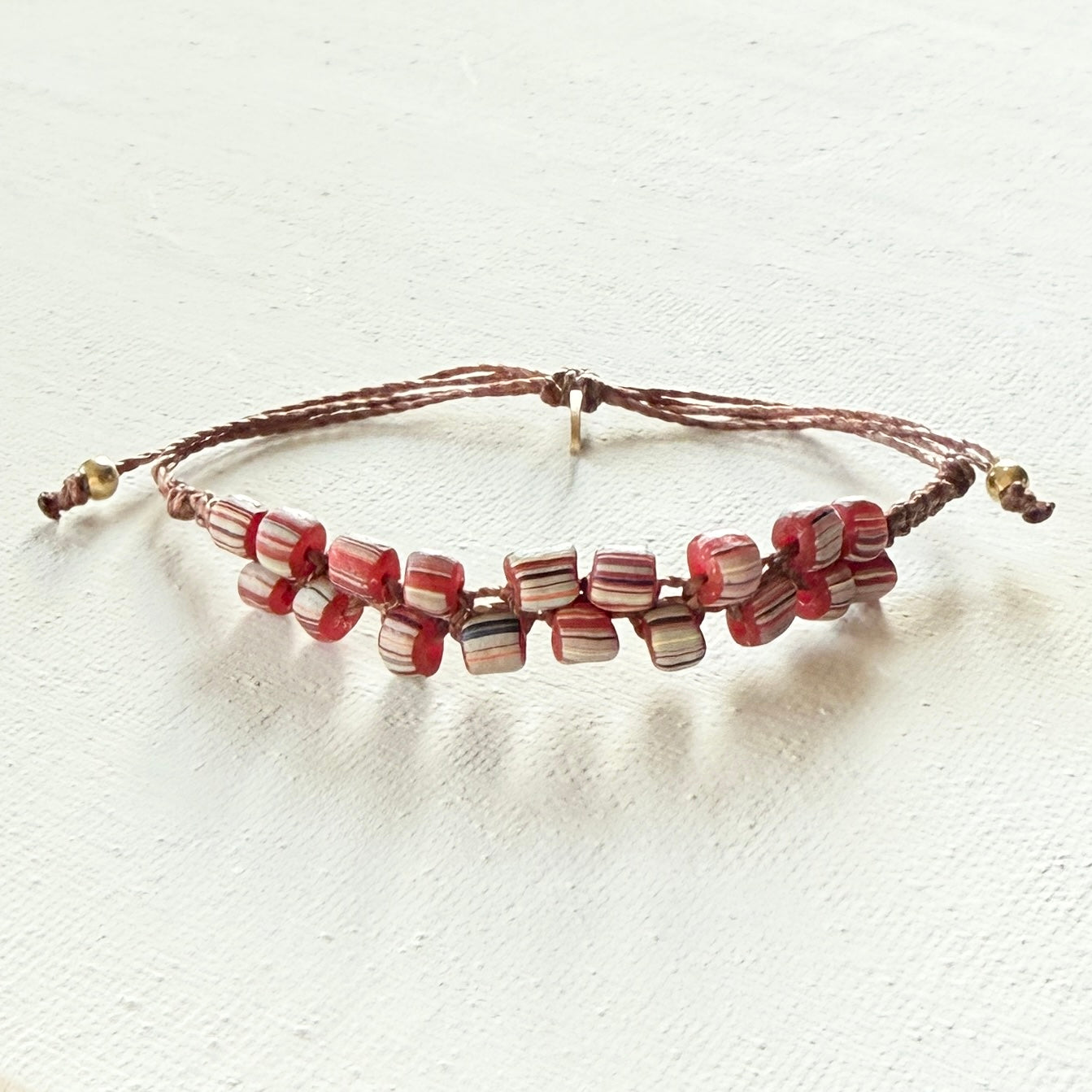 Beaded bracelet with red striped beads and  brass on a white pattern on a textured white background