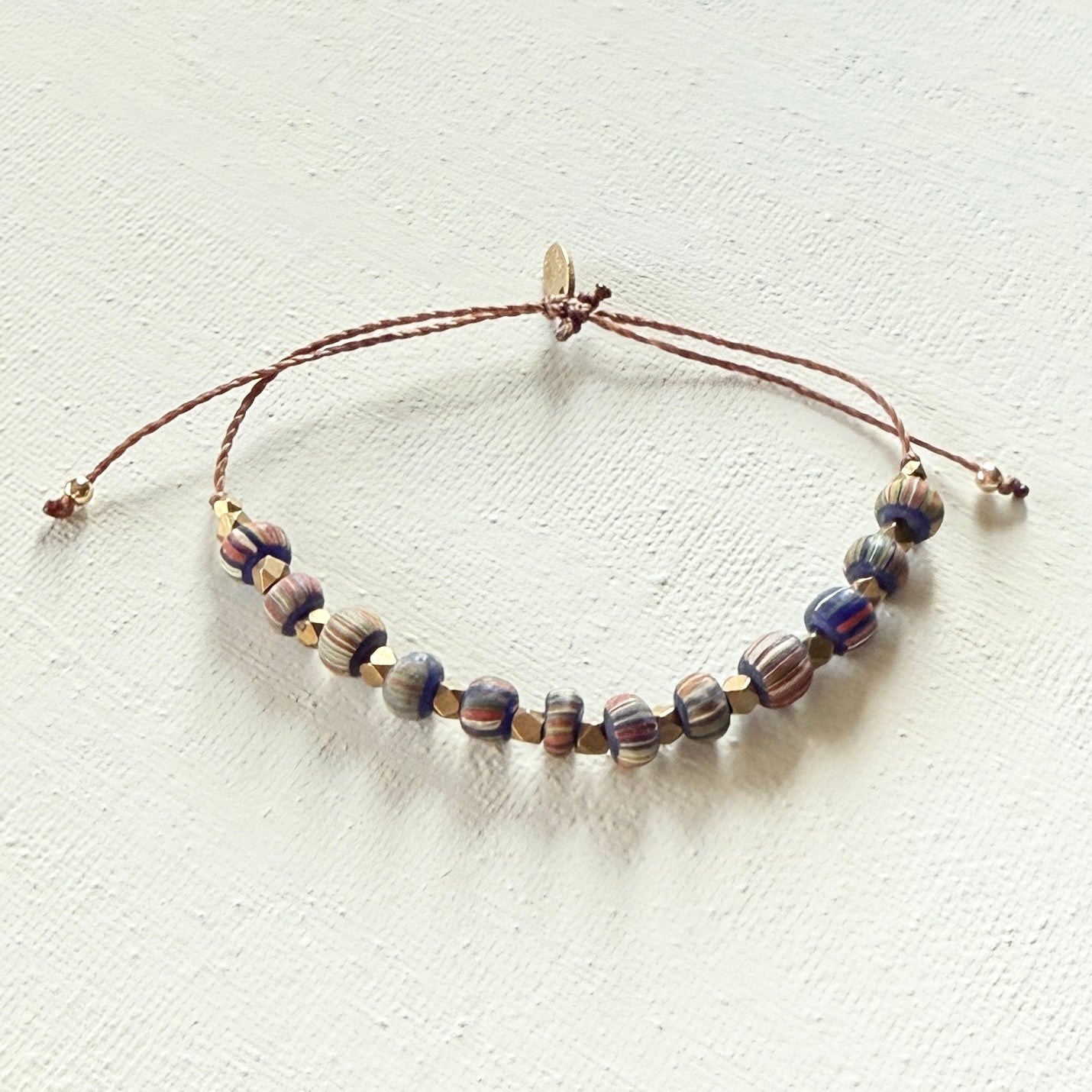 Beaded bracelet  with strips and brass beads on a brown cord on a white background