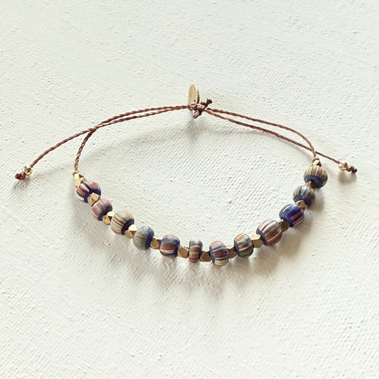 Beaded bracelet  with strips and brass beads on a brown cord on a white background