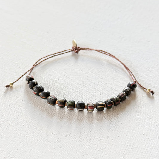 Beaded bracelet with dark beads on a thin brown cord against a light background